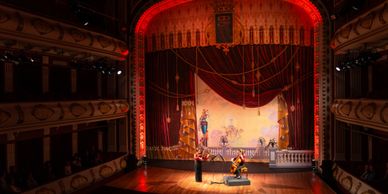 A classical music performance on an ornate theater stage with a painted backdrop.