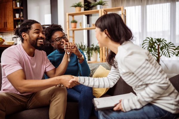 Happy couple receiving house keys and shaking hands with agent.