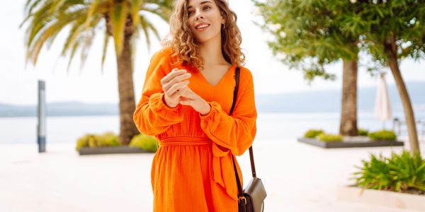 Woman in orange dress smiling outdoors by palm trees.