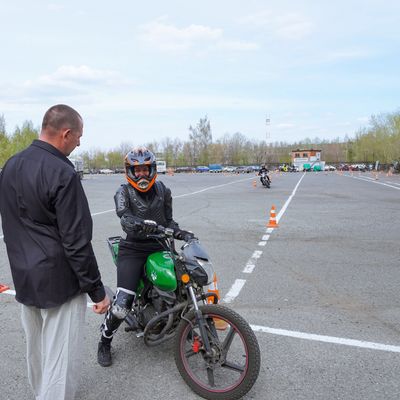 Person on motorcycle with instructor in open area.