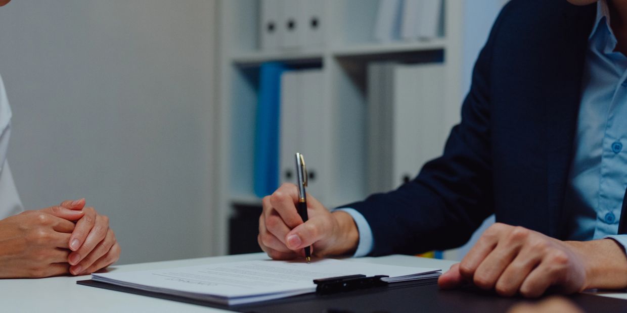 Two people at a desk, one signing a document.