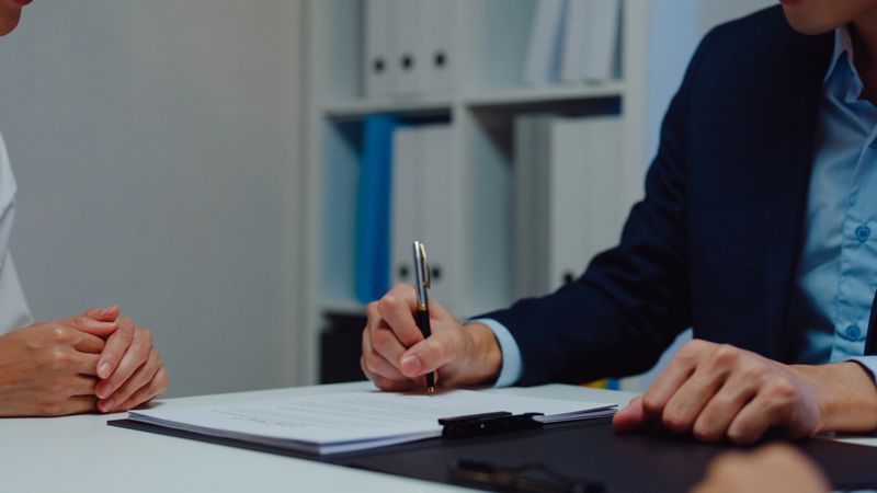 Closeup of young Asian businessman mentor corporate leader manager counselor communicate with businesswoman and sign a contract at office night. Businesspeople in workplace concept.