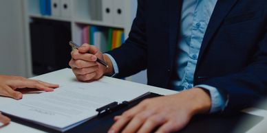 Person in suit holding pen over contract paper at desk.