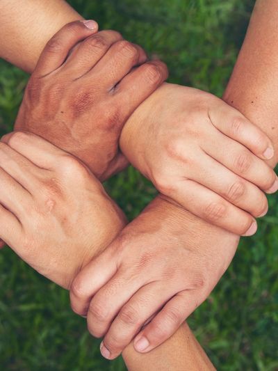 Four hands of different skin tones holding each other's wrists in unity.