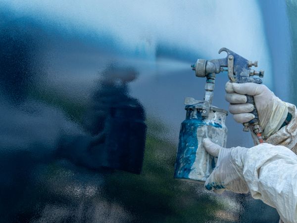 Person spraying blue paint on surface using spray gun.