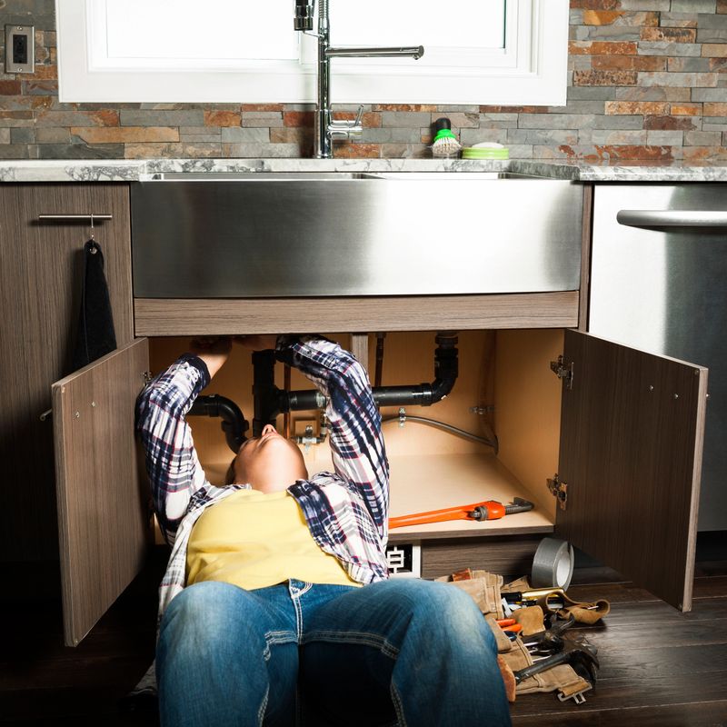 Female plumber repairing a sink in a domestic kitchen.