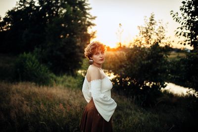 Woman enjoying a sunset in a field with arms raised.