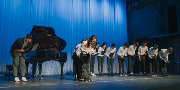 Performers bowing on stage next to a grand piano.