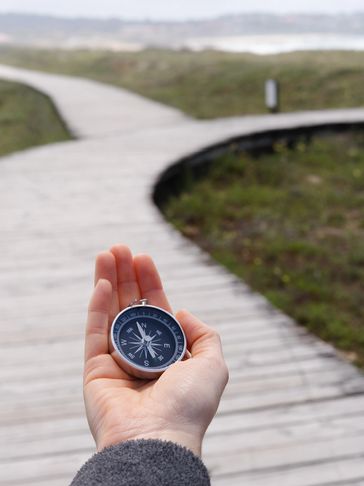 Hand holding a compass over a wooden path.