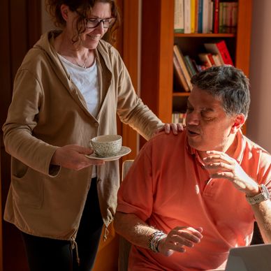 Woman offering a cup of tea to a seated man in a cozy room.