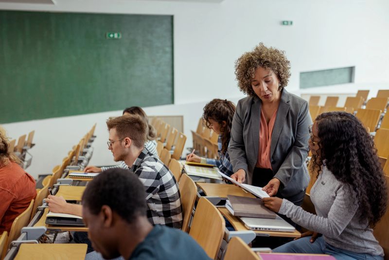 Mature Hispanic Education Teacher Handing Over Test Results to Her Students in the Classroom