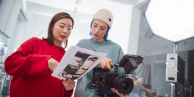 Two women examining photos near a camera on set.