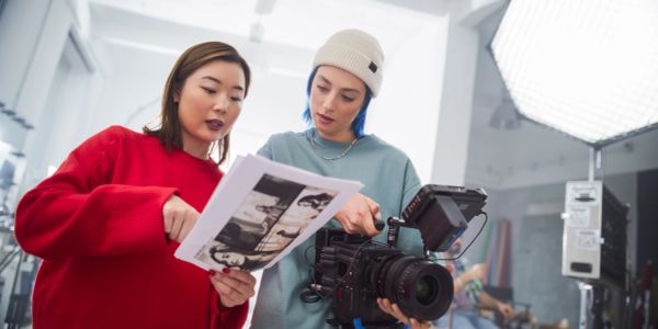 Two women reviewing film strips near a camera on set.
