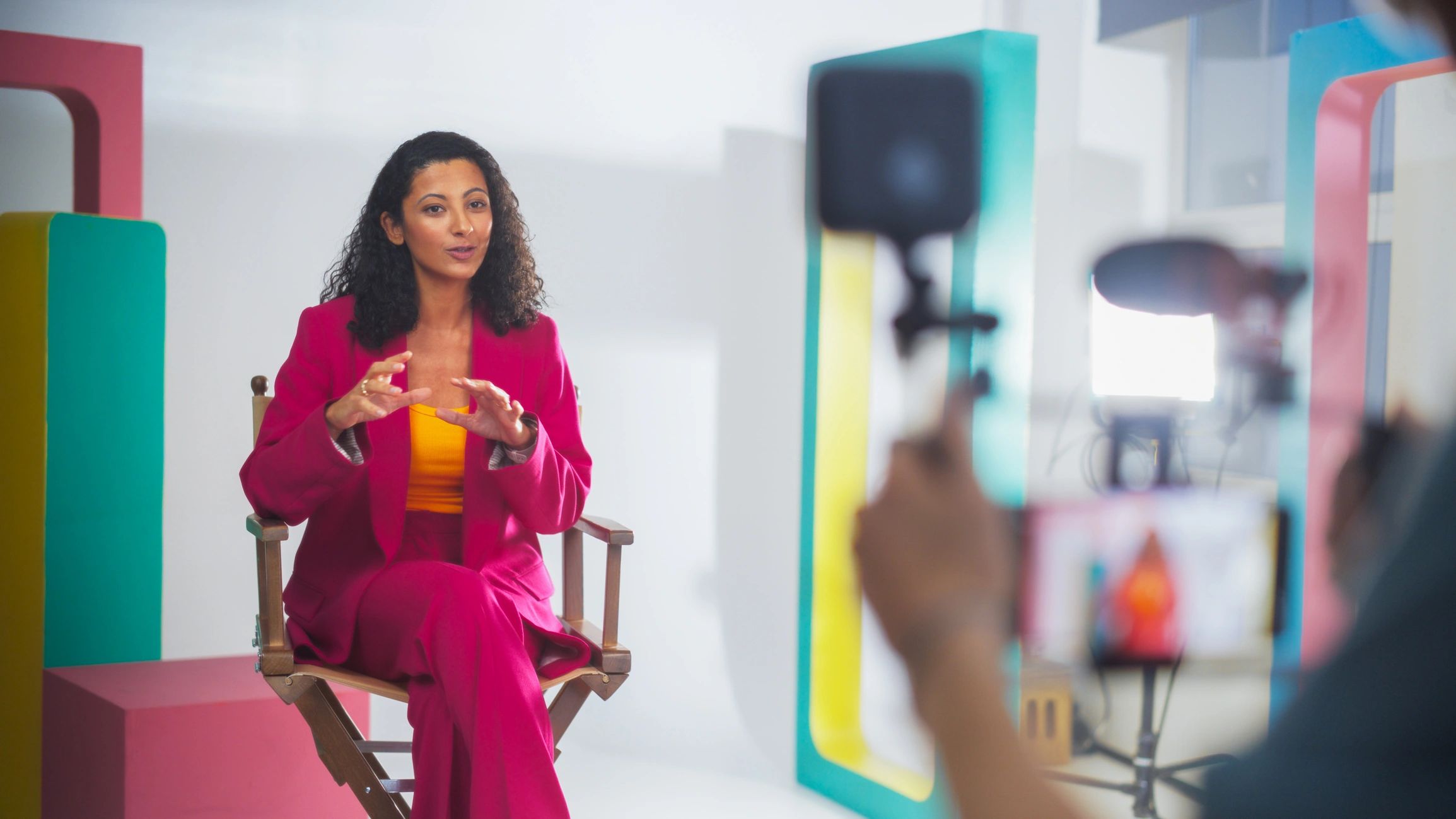 Woman in pink suit talking on camera in a studio.