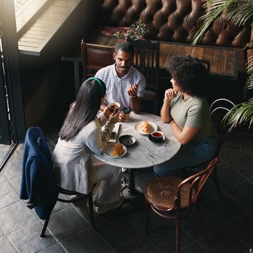 Three friends enjoying coffee and pastries at a cozy café table.