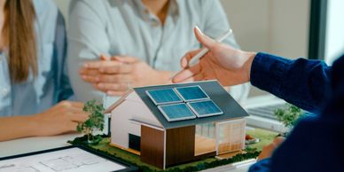 Model house with solar panels being discussed by people.