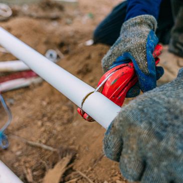 Worker cutting a white plastic pipe with a red pipe cutter.