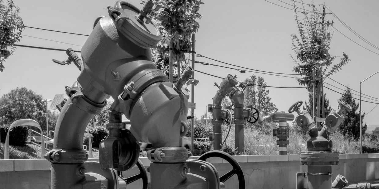 Black and white photo of large industrial water pipes and valves outdoors.