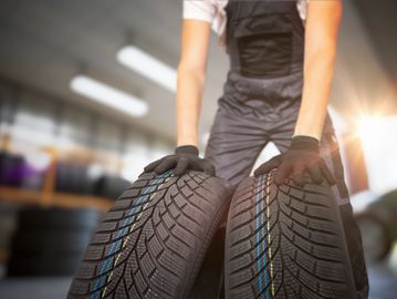 Person holding two new tires in a workshop setting.