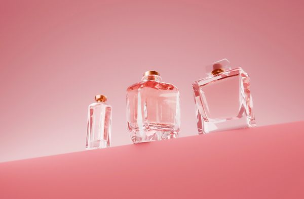 Tres frascos de perfume sobre fondo rosa.