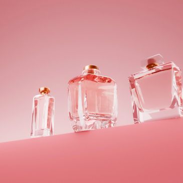 Three glass perfume bottles on a pink background.