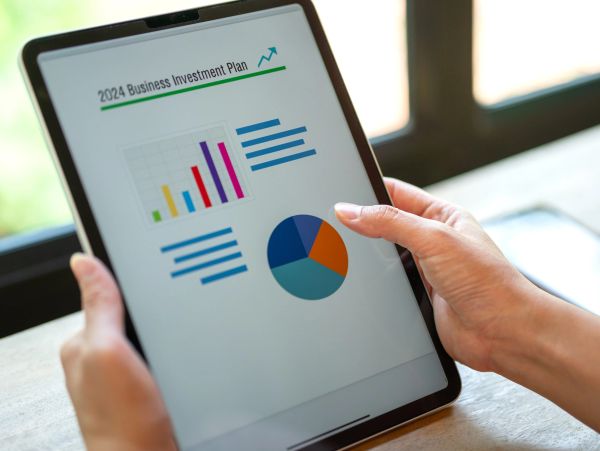 Person holding a tablet displaying a 2024 business investment plan with charts.