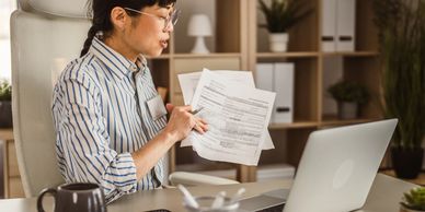 Woman working from home, holding documents and using a laptop.
