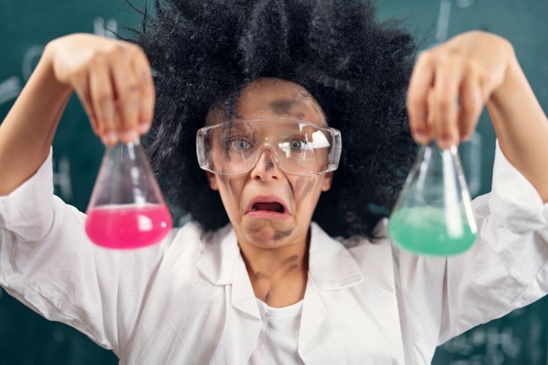 Crazy little scientist disappointed by the experiment results. The boy is holding flasks with colorful chemical substances.Shot with Nikon D850