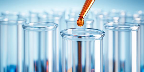 Droplet from a pipette falling into a test tube among others in a lab setting.