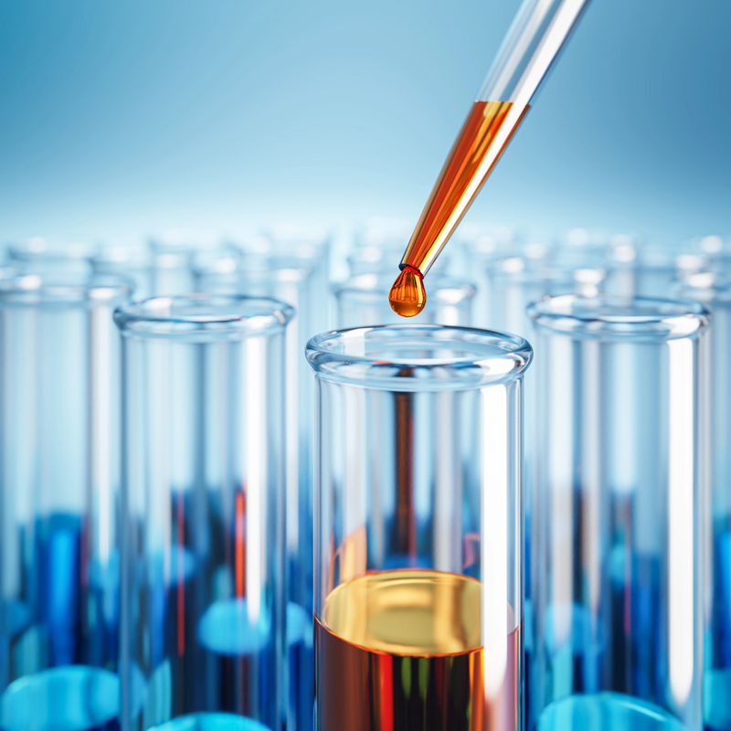 Closeup of test tubes with orange or blue liquid. Dropping glass with an orange drop above. Testing laboratory,  chemical testing facility, medical testing. Selective focus on foreground.