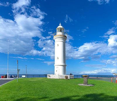 White lighthouse on a green lawn under a bright blue sky with clouds.