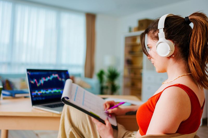 Young Businesswoman with Headphones checking Bitcoin or stock exchange price chart on digital exchange on a laptop monitor computer at her desk at home, cryptocurrency future price action prediction. Stock Bitcoin ETF Trading.