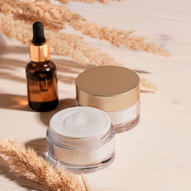 Skincare cream jars and a dropper bottle on a wooden surface with dried plants. Handmade products at Sugaring Waxing Ocala In Fruitland Park, Lady Lake, The Villages, Wildwood and leesburg, FL. Perfect for aftercare of a Brazilian Wax and Vajacial Services
