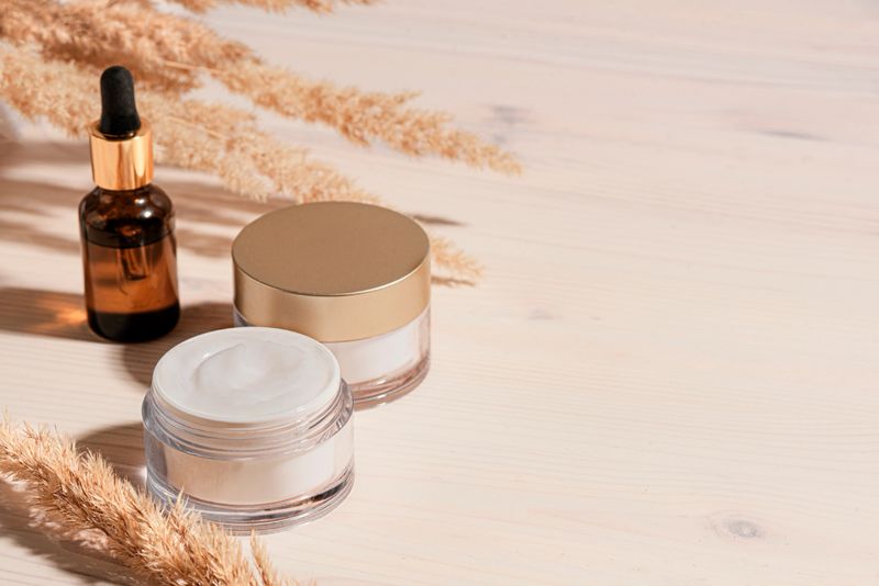Cosmetic serum and beauty cream products with dry reeds or pampas grass on wooden background, trendycomposition with hard light. Facial anti age natural skin care, copy space.