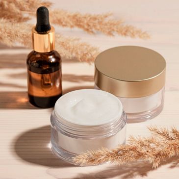 Luxury skincare cream and serum bottle with golden lids on a neutral background.
