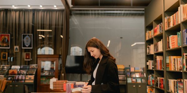 A person stands in a cozy bookstore, holding a book, with shelves lined with colorful titles in the 