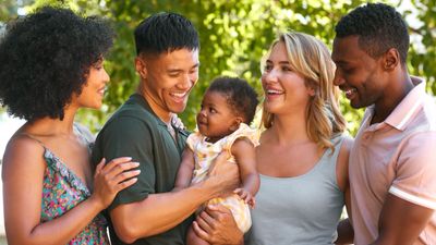 Diverse group happily admiring a baby outdoors.