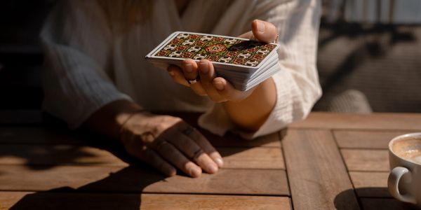 Person holding a deck of cards over a wooden table with coffee nearby.
