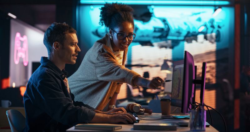 Portrait of Black Creative Director and Male Developer Talking About Work in Creative Agency. Two Stylish Diverse Employees Discussing Character Design on Computer in Game Development Company