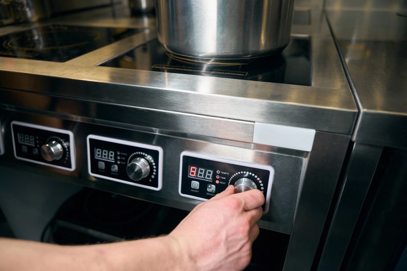 Cropped male chef turning on button of modern electric stove for heating dish in saucepan on kitchen in restaurant. Concept of tasty healthy eating