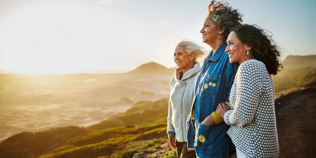Three women enjoying a scenic sunset view on a hillside.
