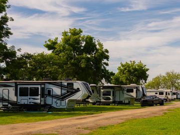 RVs at a tree-lined Georgia campground with grassy pull-through sites under a bright blue sky.