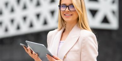 Confident woman in glasses holding a tablet and smartphone outdoors.