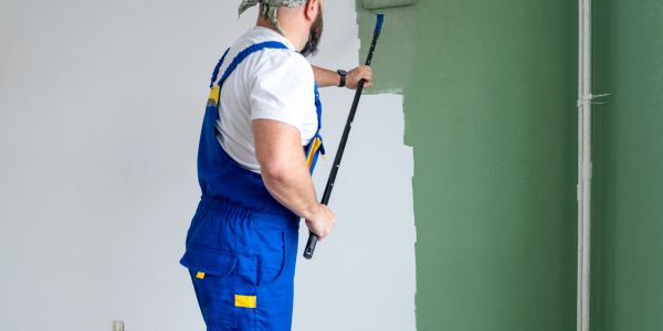 Man painting a wall green with a roller.