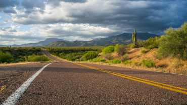 Desert road leading to mountains under a cloudy sky.