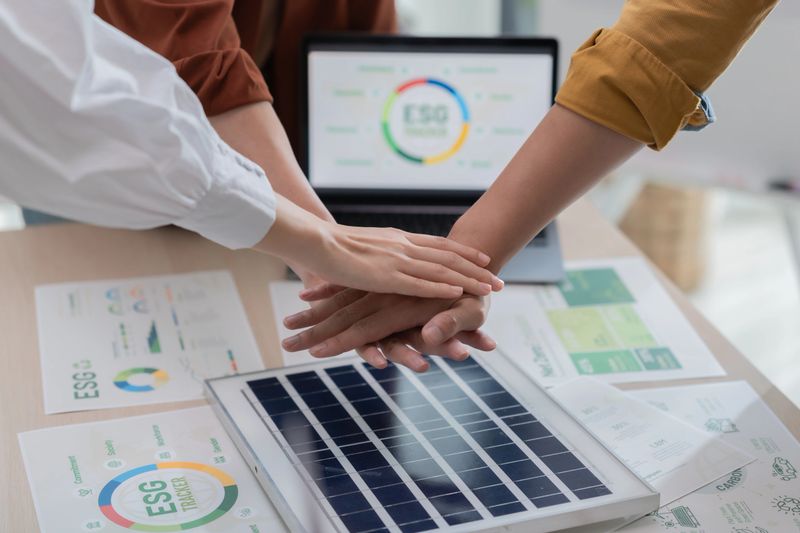 A group of young professionals stack hands, symbolizing teamwork and unity in pursuit of sustainable energy solutions during a business meeting.