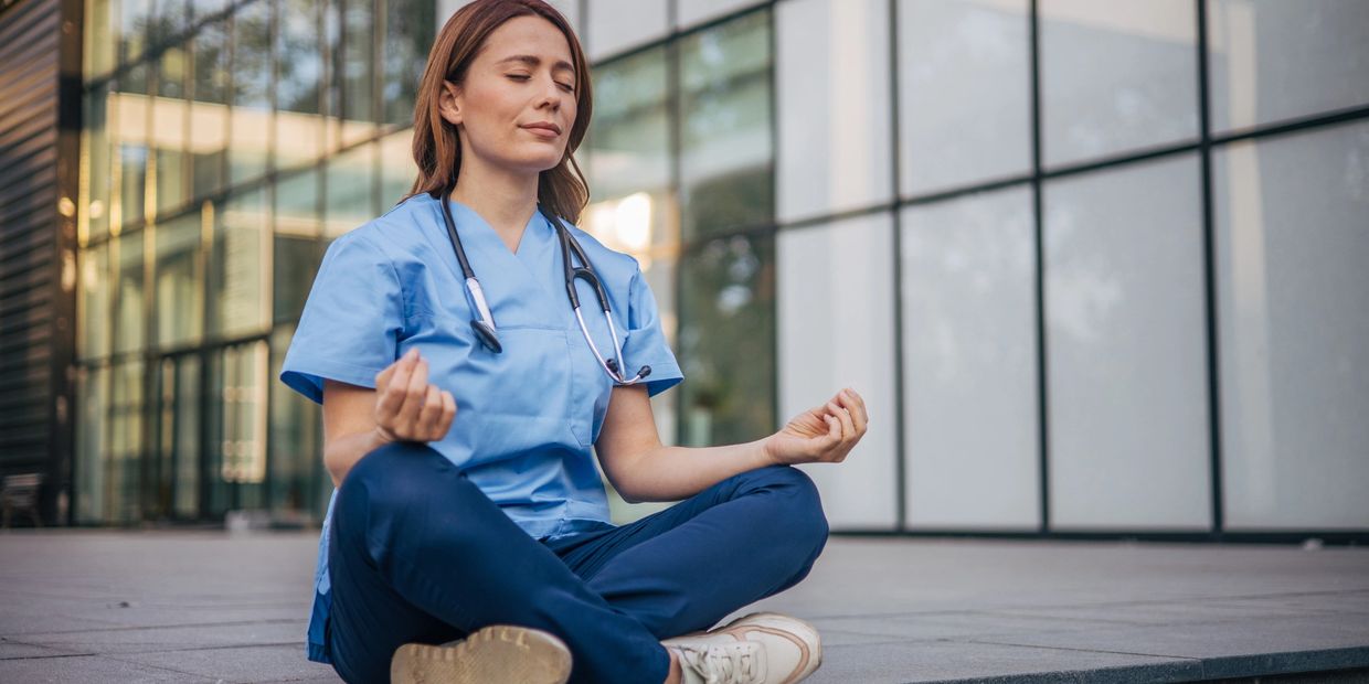 Healthcare worker meditating outdoors in scrubs.