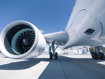 Close-up of an airplane engine and landing gear on tarmac under clear sky.