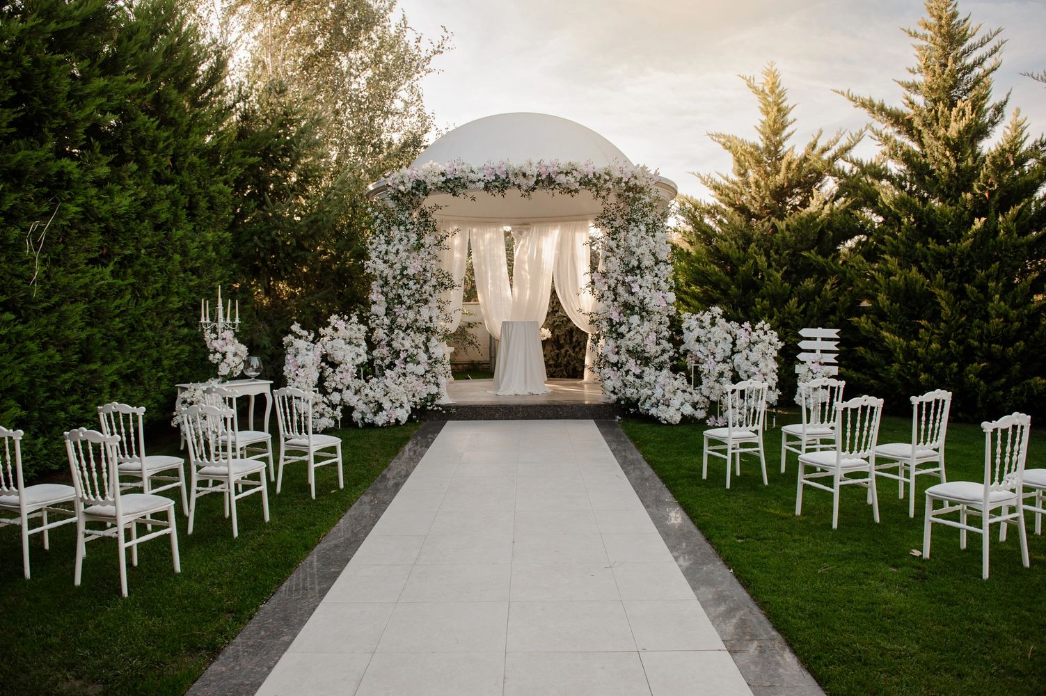 Elegant outdoor wedding setup with white chairs and floral decorations.