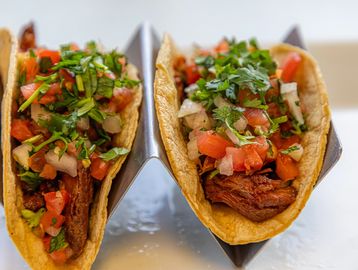 Two tacos filled with seasoned meat, fresh salsa, and chopped cilantro.